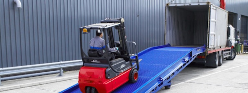 Forklift driving up mobile yard ramp into a shipping container on a lorry