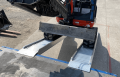 Digger driving up pair of loading ramps side view 