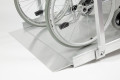 Wheelchair ramps with handrails on a slope with a wheelchair going up it. Shows the surface and foot end of the ramp close up.