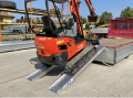Digger driving up vehicle ramps onto van 