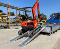 Digger driving up pair of loading ramps resting on van 