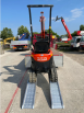 Digger driving up pair of alloy loading ramps 
