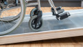 Close up of a wheelchair ramp without handrails to show the grip surface. A wheelchair is being pushed up the ramp which is resting on a step.