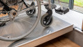 Close up of a wheelchair ramp without handrails to show the grip surface. A wheelchair is being pushed up the ramp which is resting on a step.