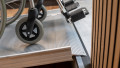 Close up of a wheelchair ramp rest on connection with pre-drilled holes. A wheelchair is being pushed up the ramp which is resting on a step.