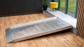 Full view of a wheelchair ramp without handrails which is resting on a step.