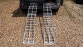 pair of motorbike ramps with support legs resting on the back of a vehicle ready to use for loading