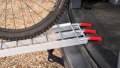 single motorbike ramps with support legs resting on the back of a vehicle with a push bike being loaded - close up of red, finger style rest on connection