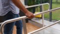 A close up of the handrails of our wheelchair ramps with handrails. A pedestrian is walking up and holding onto the handrails