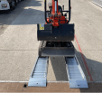 Front view Digger driving up plant ramps resting on flat bed van