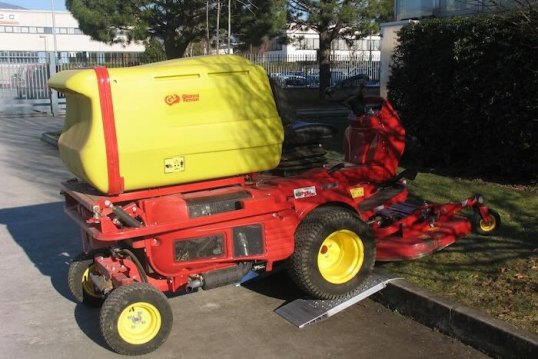 Ride-on lawnmower driving up aluminium container ramps over kerb 