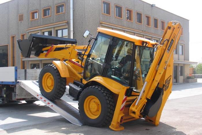 Rubber tracked machine driving up pair of aluminium loading ramps into flat bed vehicle