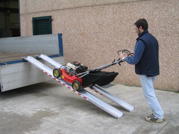 Man pushing lawnmower up pair of van ramps 