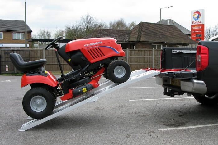 Ride-on lawnmower going up a pair of ramps into flat bed vehicle