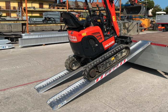 Rubber tracked machine driving up pair of aluminium loading ramps 