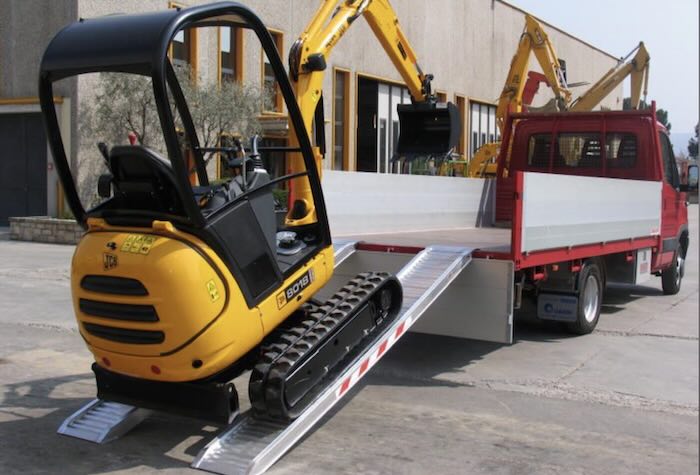 Rubber tracked machine driving up pair of aluminium loading ramps 