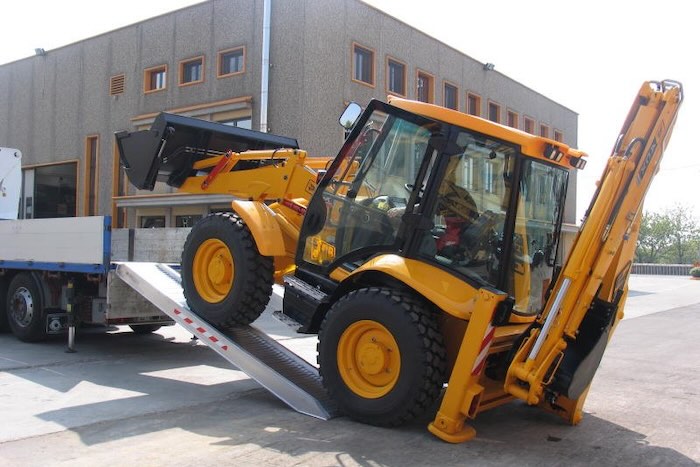 Rubber tracked machine driving up pair of aluminium loading ramps 