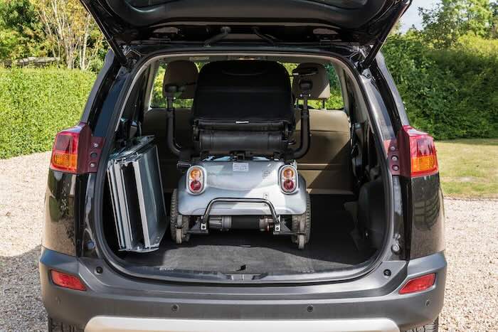 Folded mobility scooter ramps in car boot next to mobility scooter