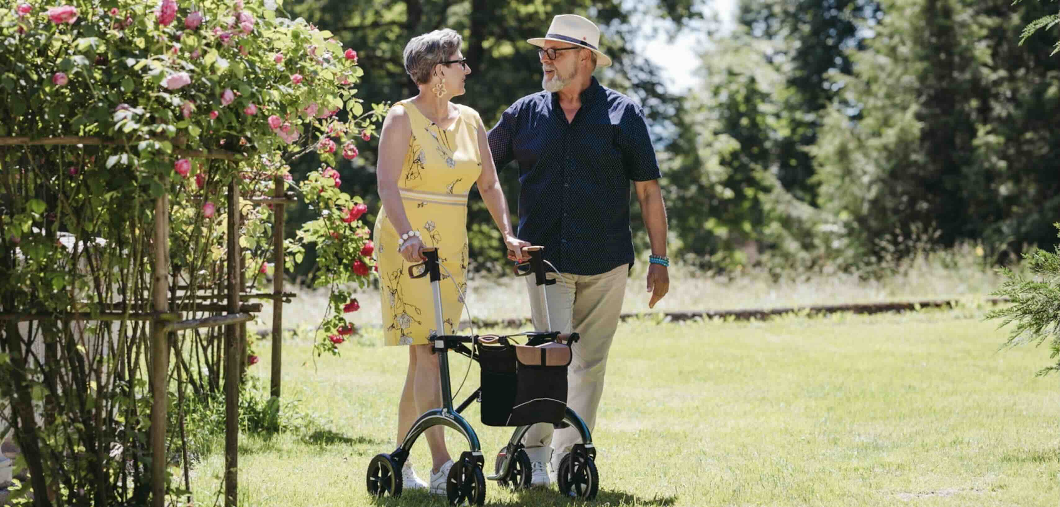 Lady and man walking in garden, lady using Saljol Carbon Rollator