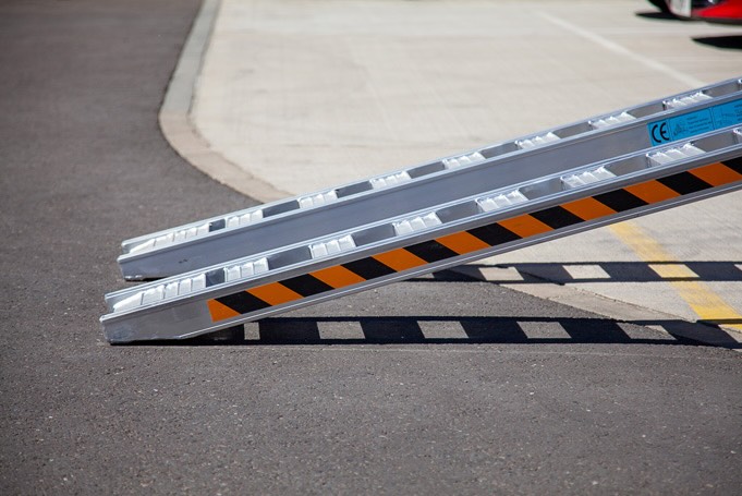 Rubber tracked machine driving up pair of aluminium loading ramps 