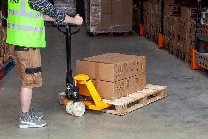 Warehouse worker using manual pallet truck with nylon wheels to move a pallet 