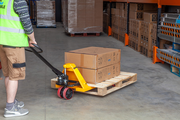 Warehouse worker using manual pallet truck to move a pallet 