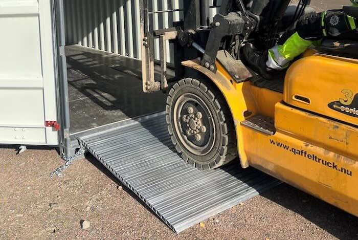Forklift driving up aluminium ramp into container