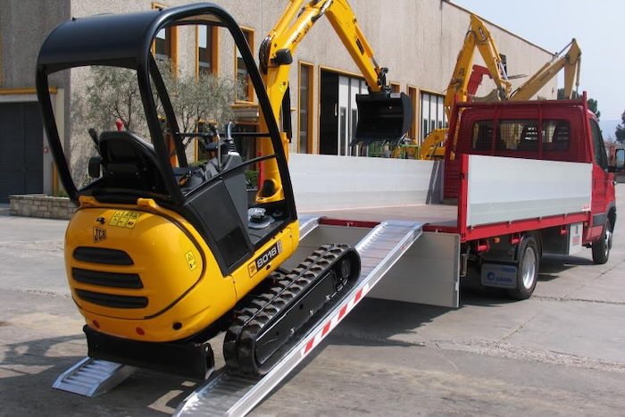 Digger driving up a pair of ramps onto a van