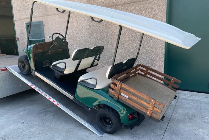 Golf buggy driving up pair of ramps into flat bed vehicle 