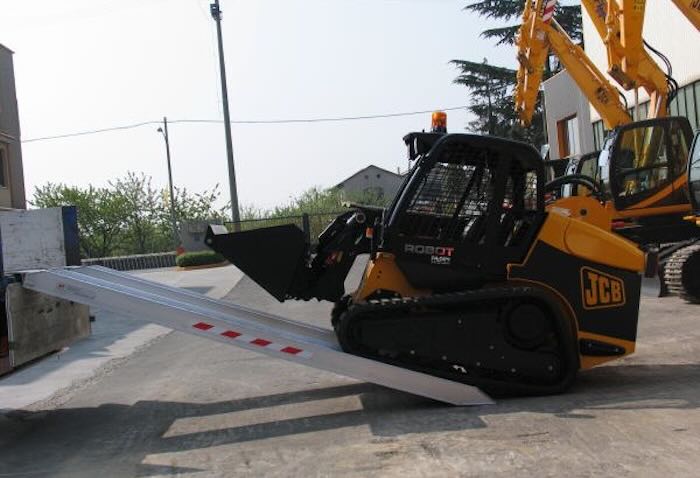 Rubber tracked machine driving up pair of aluminium loading ramps 