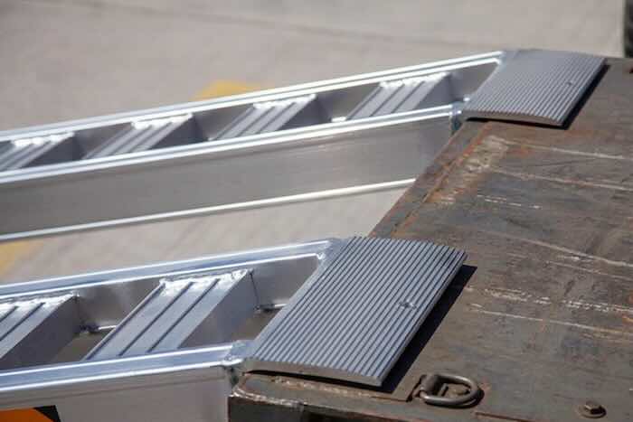 Rubber tracked machine driving up pair of aluminium loading ramps into flat bed vehicle