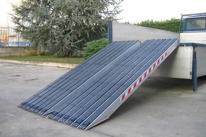 Pair of heavy duty loading ramps with rubber surface resting on flat bed vehicle 