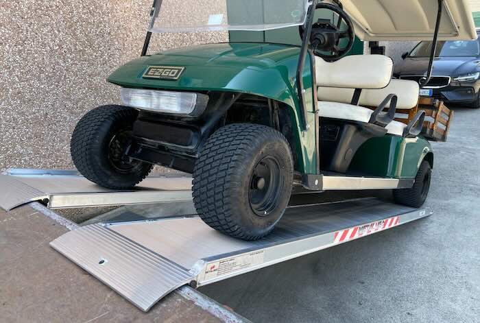 Golf buggy driving up a pair of loading ramps 