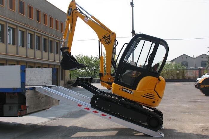 Rubber tracked machine driving up pair of aluminium loading ramps 