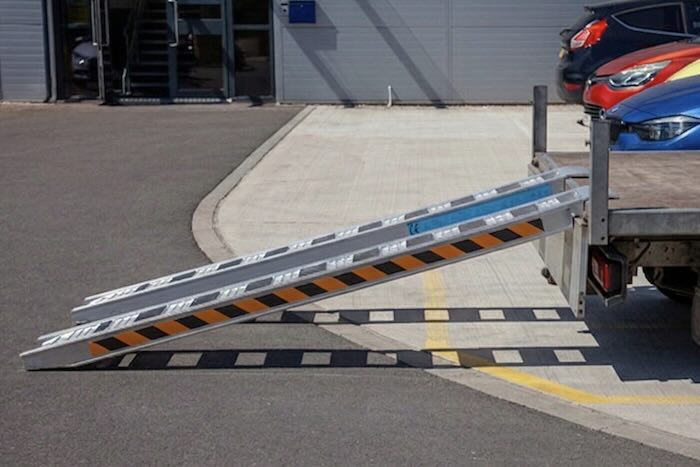 Rubber tracked machine driving up pair of aluminium loading ramps 