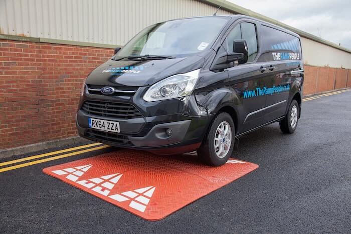 Van driving over red speed cushion on tarmac road 