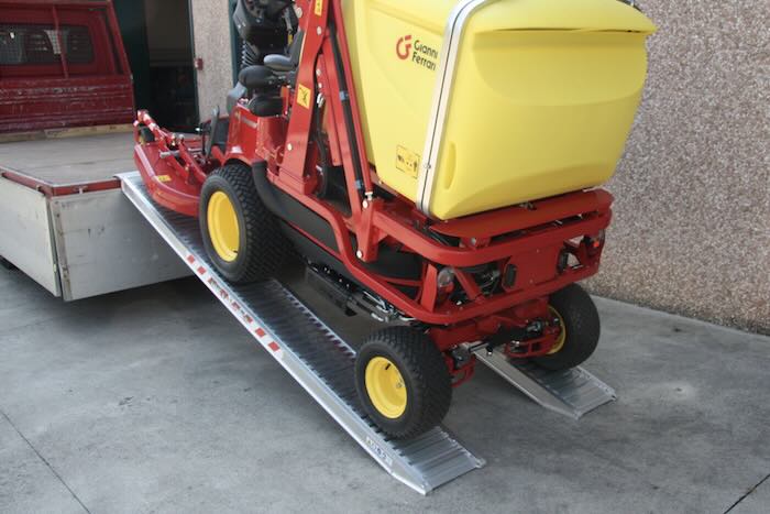 Ride on mower driving up pair of aluminium loading ramps into flat bed vehicle