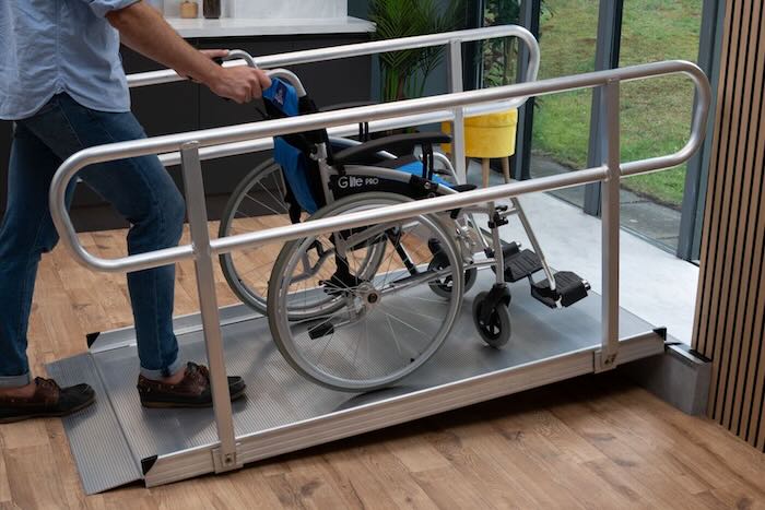 Person pushing a manual wheelchair up a wheelchair ramp with handrails to overcome step