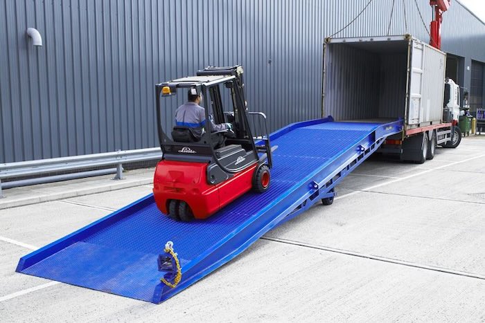Forklift driving up yard ramp into container